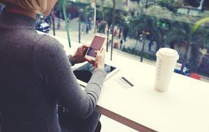 Junge Dame mit Kaffee beim Onlinebanking mit Smartphone und Tablet